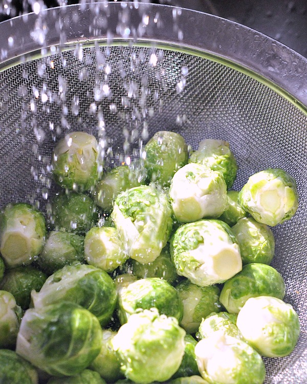 Brussels sprouts being rinsed in a mesh strainer, water sprinkled over them