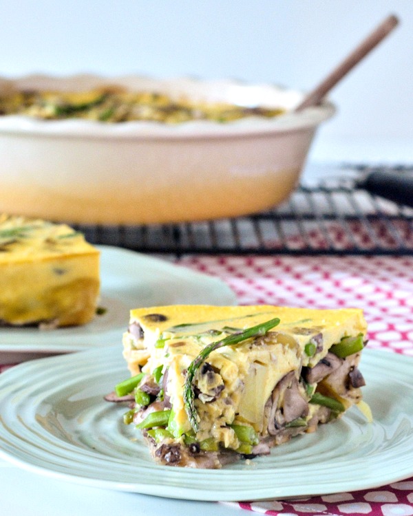 one slice of vegan mushroom quiche on a pastel green plate, the rest of the quiche in a deep pie dish blurred in background