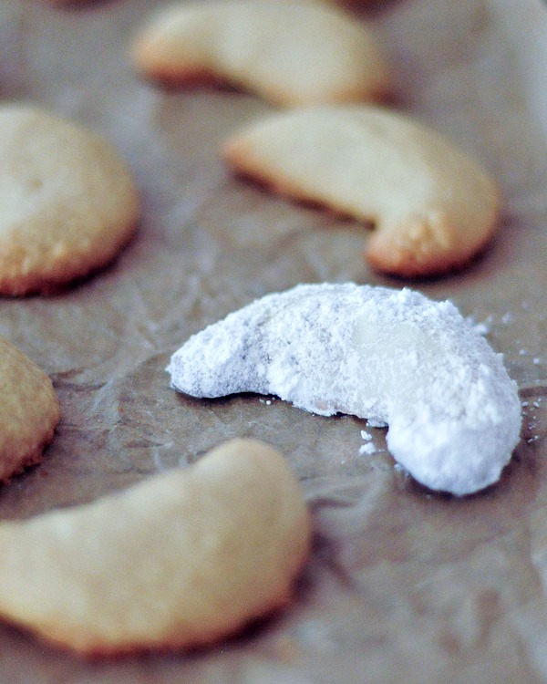 powdered sugar covered crescent shaped cookies on a baking sheet