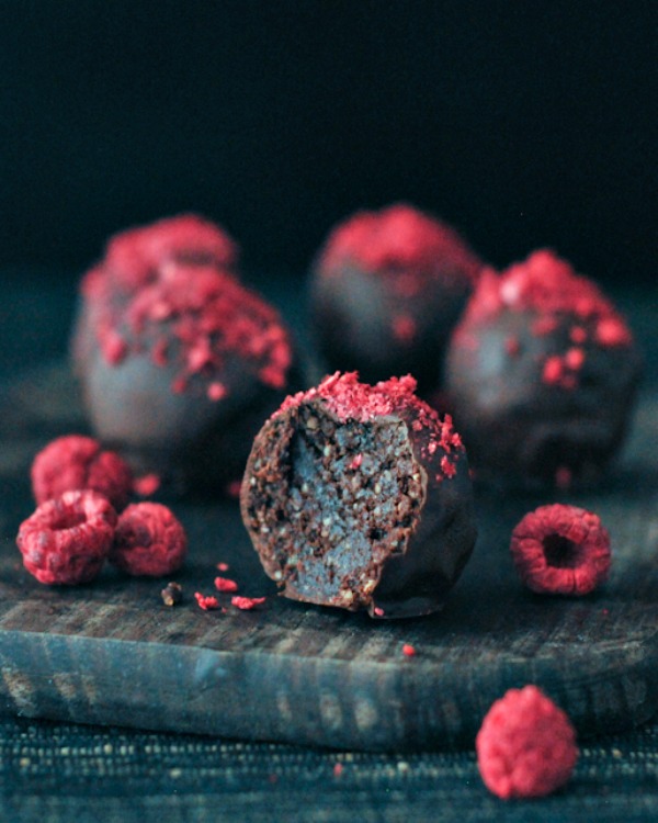 Raspberry Dusted Chocolate Fudge Brownie Truffles on a dark wood board against a dark backgruond