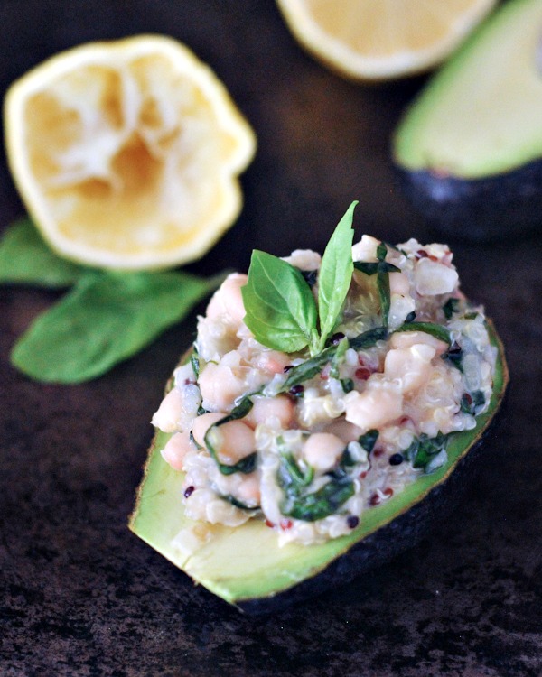 lemon basil quinoa stuffed into a half avocado, garnished with fresh basil leaf. squeezed half lemon in background.