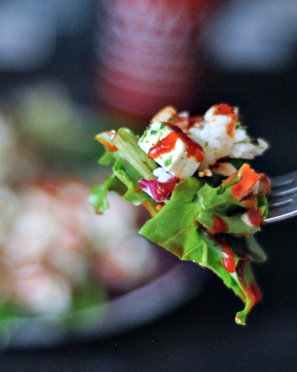 a bite of green salad with diced tofu, sriracha, and furikake flakes on a fork.
