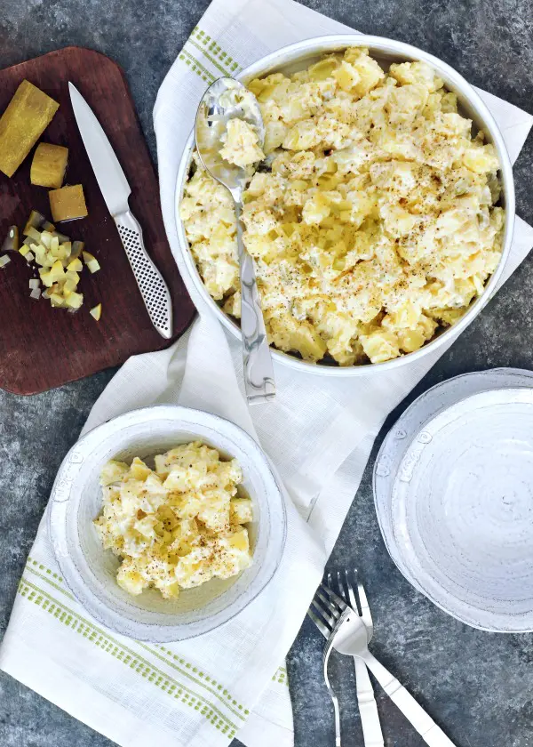 overhead view of classic vegan pickle potato salad in bowls, diced pickles with knife on cutting board