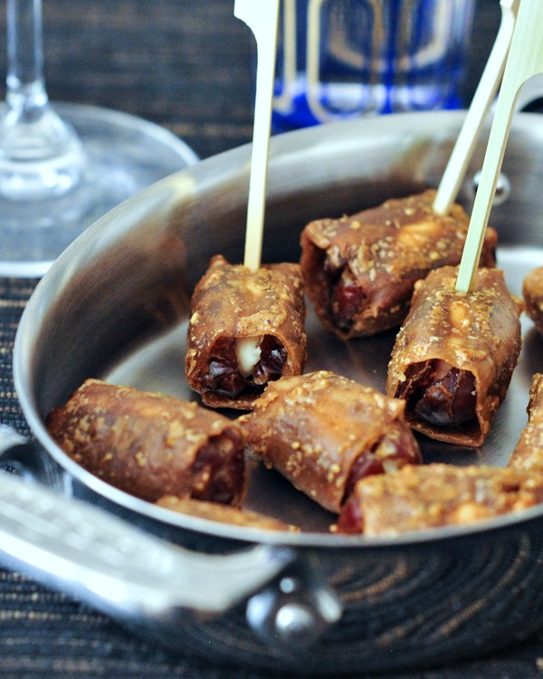 Vegan Goat Cheese Bacon Wrapped Dates on a serving platter with toothpicks and cocktail glasses in background