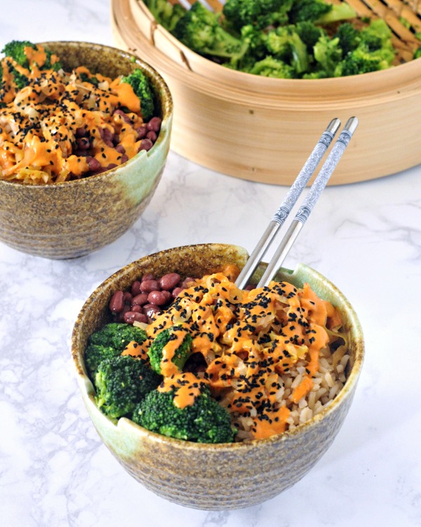 two kimchi bowls with beans, rice, broccoli, and red curry almond sauce, broccoli in bamboo steamer on the side