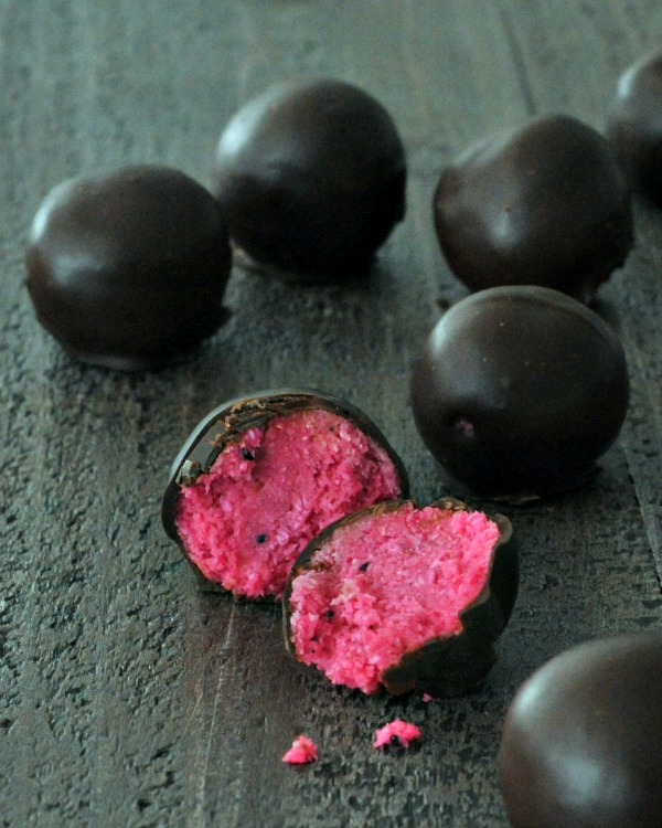 Dark Chocolate Dragon Fruit Coconut Treats arranged on a slab, with one sliced in half to show pink center