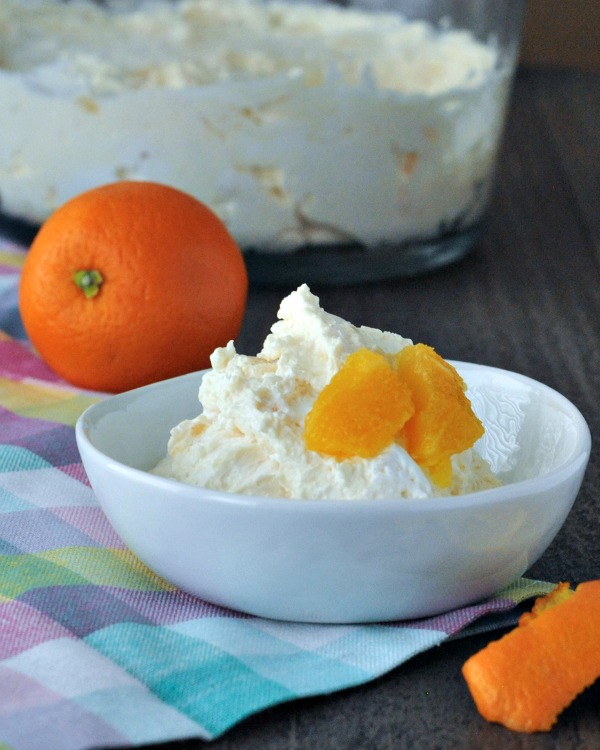 jello salad served in a white bowl, topped with fresh orange segments, full orange fruit in peel in background