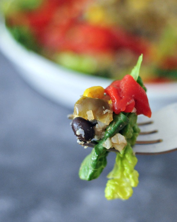 one bite of veggie burrito bowl on a fork: greens, red pepper, corn, black bean