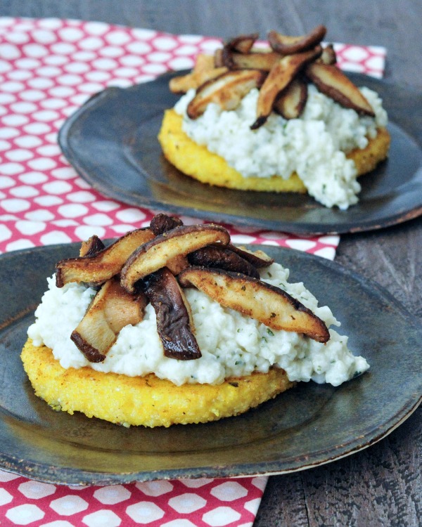 fried polenta rounds topped with cauliflower risotto and sautéed shiitake mushroom slices, sitting on a small rustic grey dish on a red and white cloth napkin.