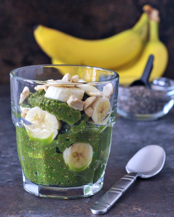 bright green pineapple chia pudding in a glass with banana slices. the green color comes from fresh spinach added for protein.