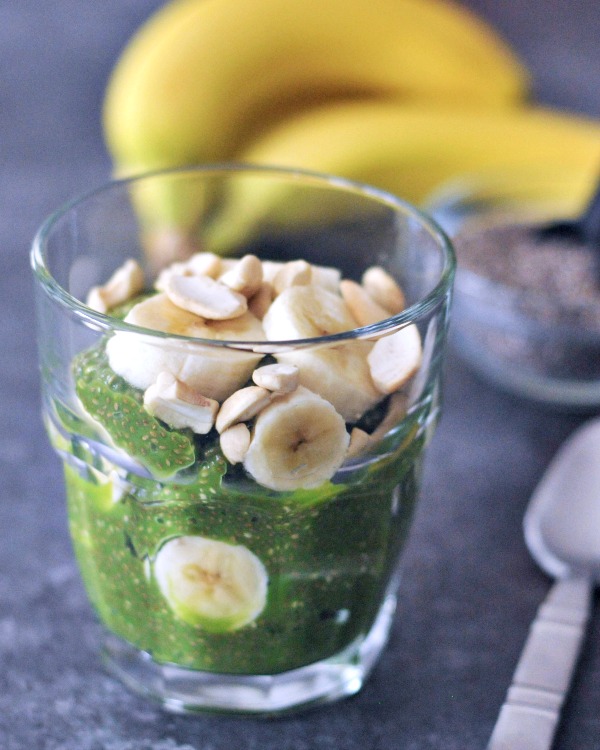 overhead view of spinach green pineapple protein chia pudding in a glass with banana slices and cashews