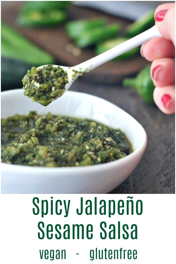 small white spoon of spicy jalapeño sesame salsa held over a small white ceramic bowl of salsa