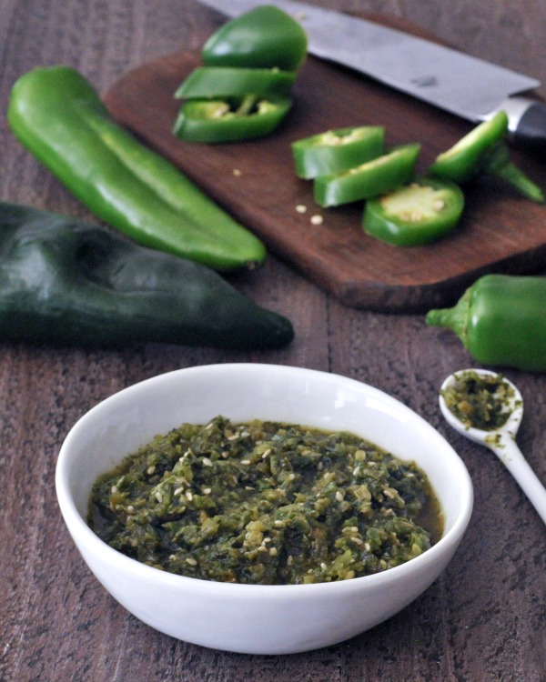 Spicy jalapeño sesame salsa in a bowl, fresh peppers and knife on a cutting board in background