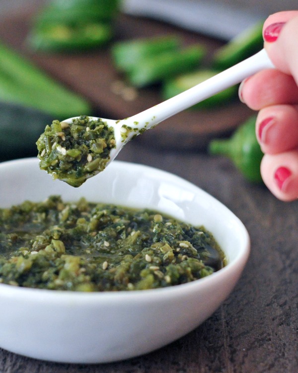 small white spoon of spicy jalapeño sesame salsa held over a small white ceramic bowl of salsa