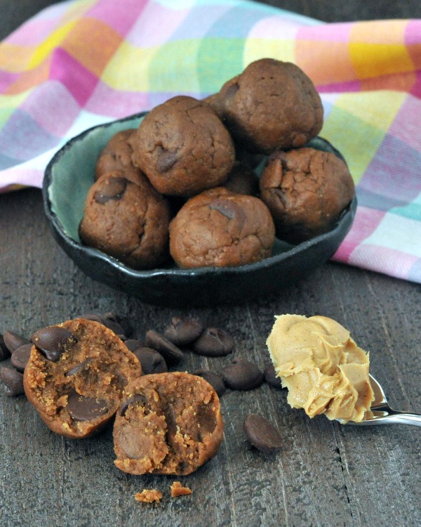 Triple Almond Cookie Dough Bites in bowl, single bite sliced open in front, with spoonful of almond butter and chocolate chips scattered about