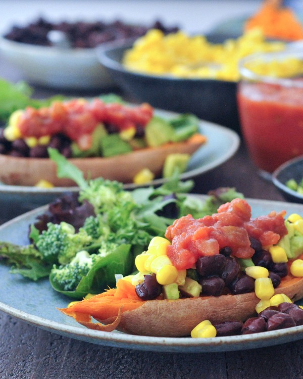 Savory sweet potato boats on plates: black bean, corn, and salsa fillings in bowls in background