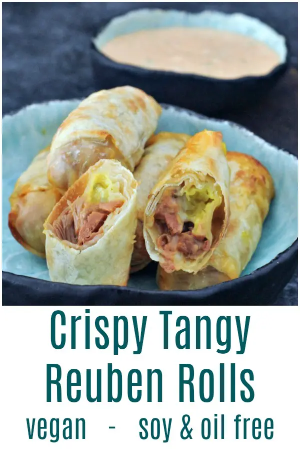 reuben rolls (jackfruit reuben sandwich filling wrapped in egg roll wrapper) in a shallow blue bowl on a darker blue background, smaller blue bowl of thousand island dressing on the side.