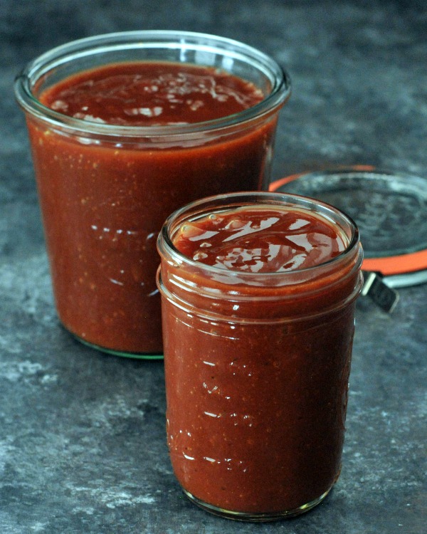two glass jars of a gluten free vegan BBQ sauce sitting on a dark grey marble countertop.