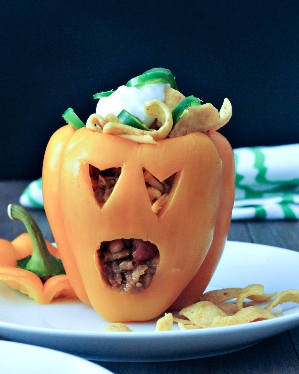a bell pepper carved into a halloween jack o lantern, filled with Frito pie (chili and fritos)