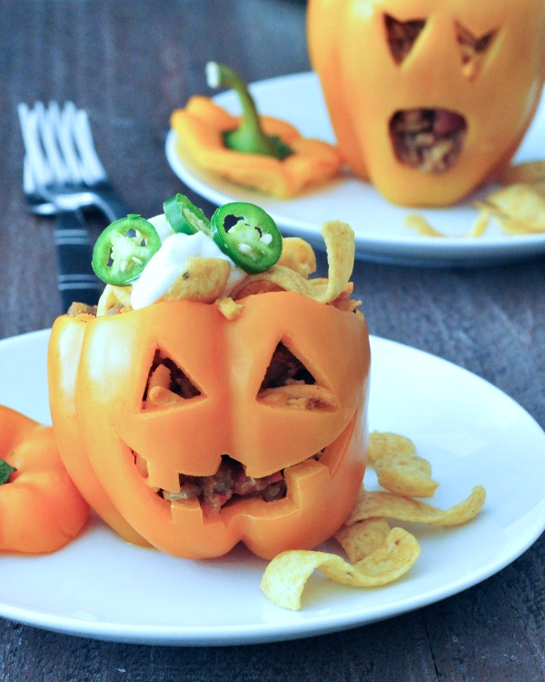 two orange bell peppers carved into a halloween jack o lantern, filled with Frito pie (chili and fritos)