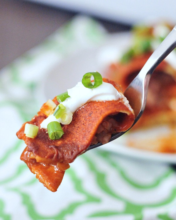 one bite of a Bean and Cauliflower Rice Enchilada on a fork, with a blurred background of a plate of enchiladas