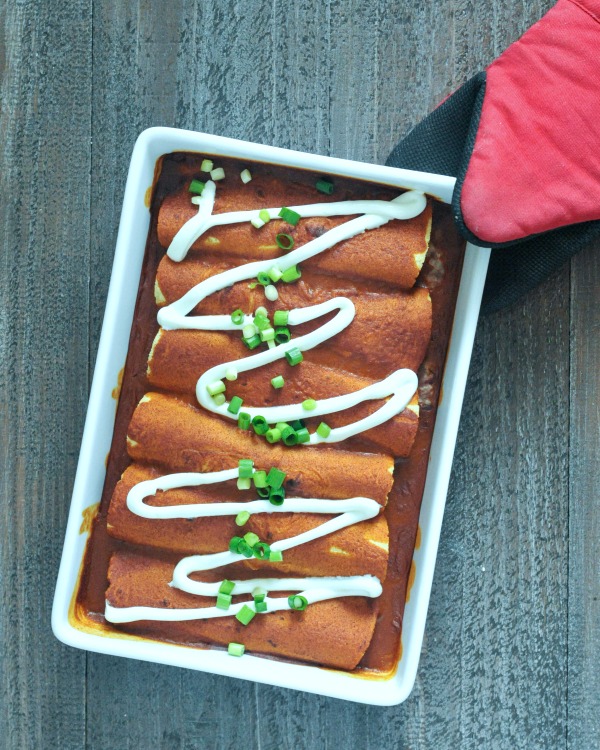 overhead view of Easy Bean and Cauliflower Rice Enchiladas in a white rectangle ceramic baking dish held by a red oven glove