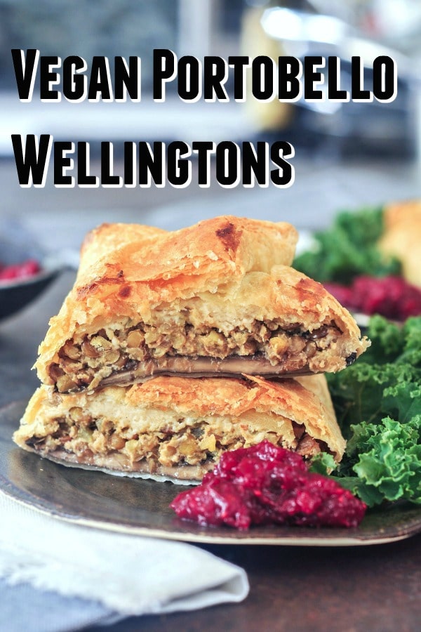 Individual portobello wellington cut in half and stacked on a dark grey plate to show inside filling of lentil veggie stuffing, kale salad and bright red cranberry sauce on the side