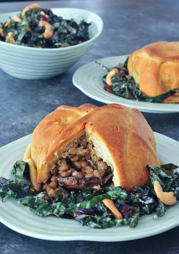 Individual portobello wellington on light green plates, cut open to show inside filling of lentil veggie stuffing, served on top of kale salad