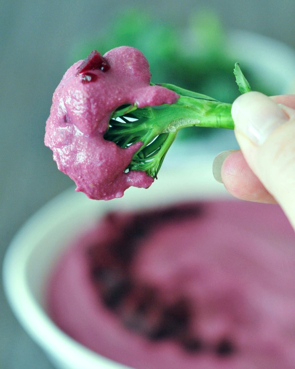 bright green piece of broccoli dipped into pink Pickled Beet Hummus 