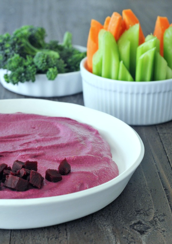 bright pink Pickled Beet Hummus in a bowl, with broccoli, carrots, and celery for dipping