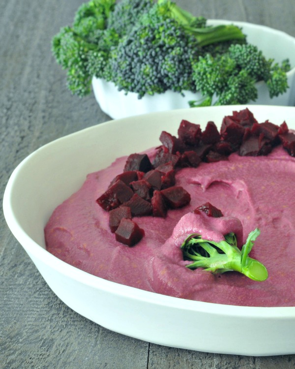 bright pink Pickled Beet Hummus in a bowl, with broccoli for dipping
