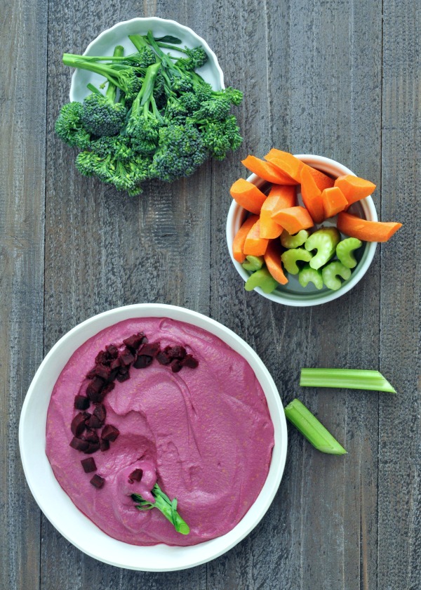 bright pink Pickled Beet Hummus in a bowl, with broccoli, carrots, and celery for dipping