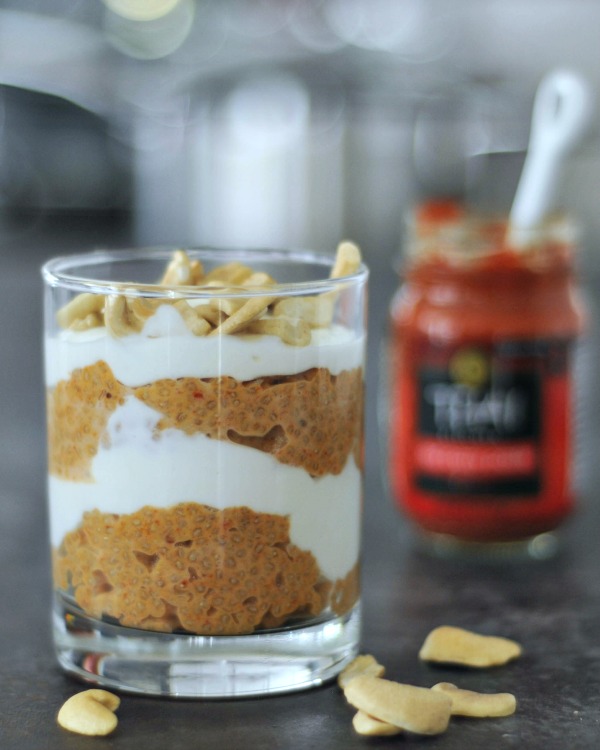 red curry coconut chia pudding and cashew cream layered in a glass, red curry paste jar in background