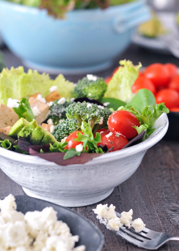 a salad in a bowl: greens, tofu cubes, tomatoes, broccoli