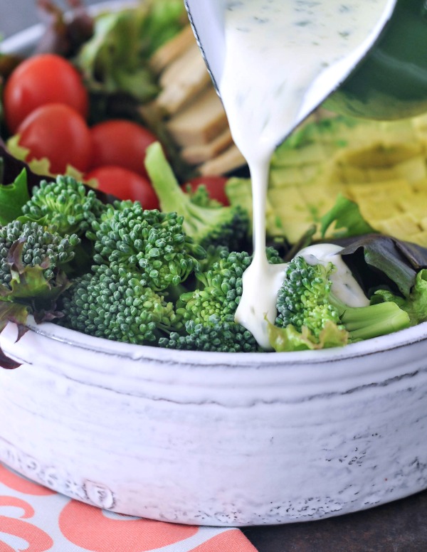 close up of ranch dressing being poured over a salad in a bowl, focused on broccoli
