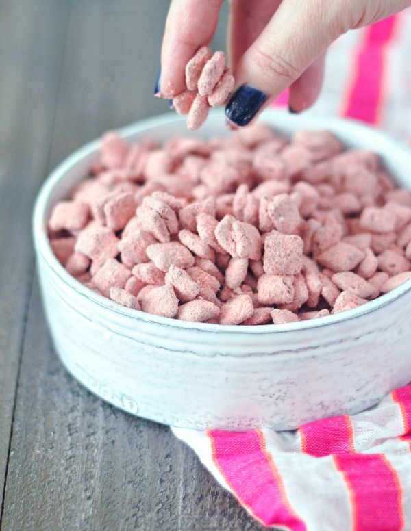 hand reaching in to bowl of Powder Pink Strawberry Puppy Chow (a strawberry powder and chocolate coated cereal treat)