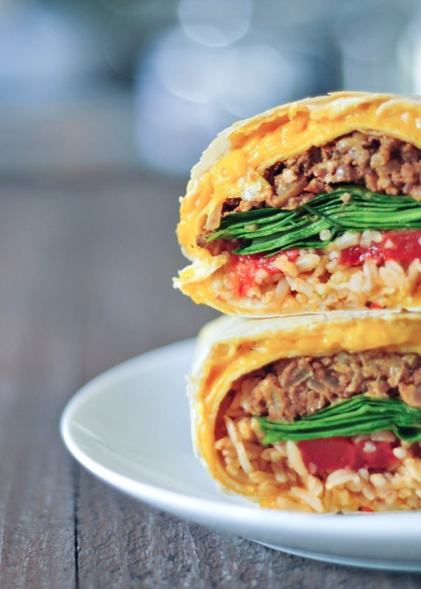 close up of a cheesy quesarito sliced in half and stacked to show insides - rice, beans, spinach, and tomato salsa wrapped in a cheese layer of quesadilla.