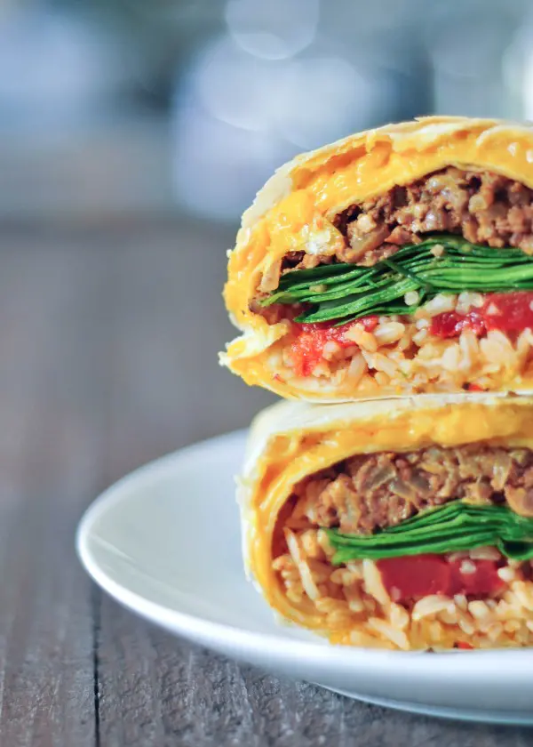 close up of a cheesy quesarito sliced in half and stacked to show insides - rice, beans, spinach, and tomato salsa wrapped in a cheese layer of quesadilla.