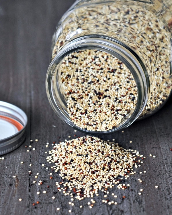 glass jar on its side, dry quinoa spilling out onto wood board.