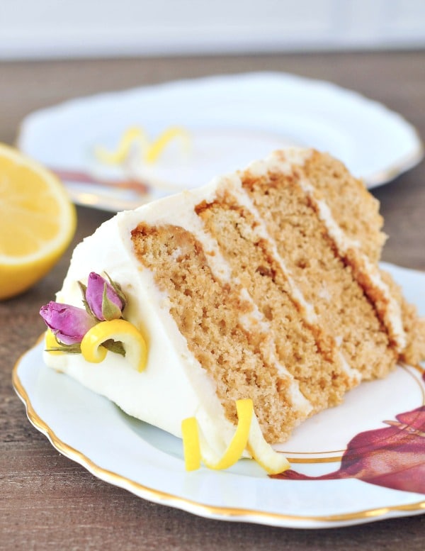 single slice of Vegan Lemon Elderflower Cake, garnished with yellow lemon peel curls and pink edible dried flowers