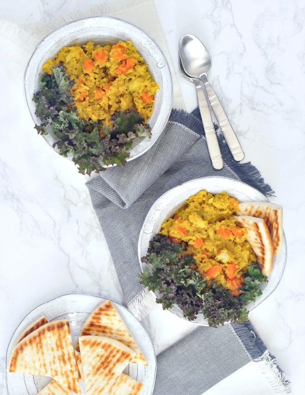 overhead view of two bowls of yellow kitchari and kale. 