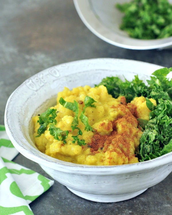 close up of turmeric yellow kitchari and fresh kale in a bowl with a green and white napkin alongside.