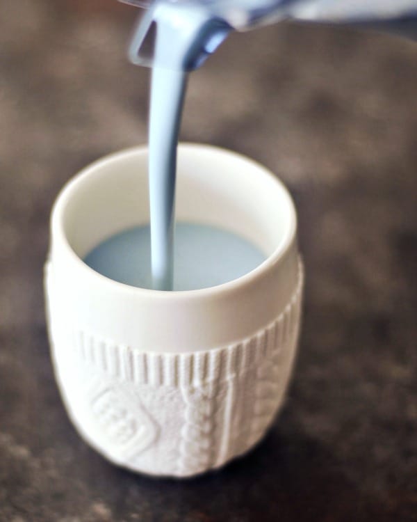 pale blue vanilla mint cashew milk being poured into a white mug