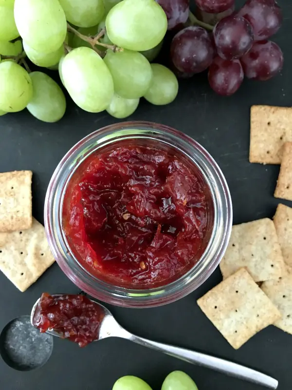 jar of easy tomato refrigerator jam on a snack tray with grapes, crackers