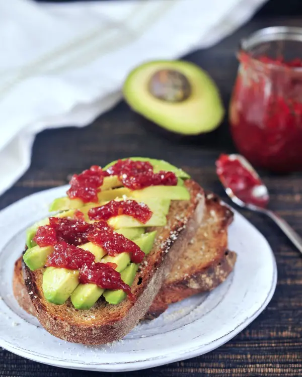 tomato jam on avocado toast, half avocado and jar of jam in background