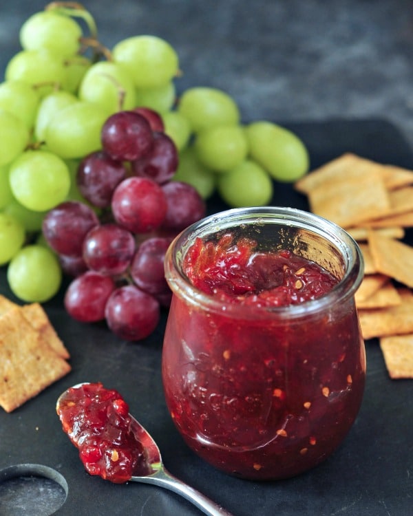 open jar of Easy Tomato Refrigerator Jam on a snack tray with crackers and grapes