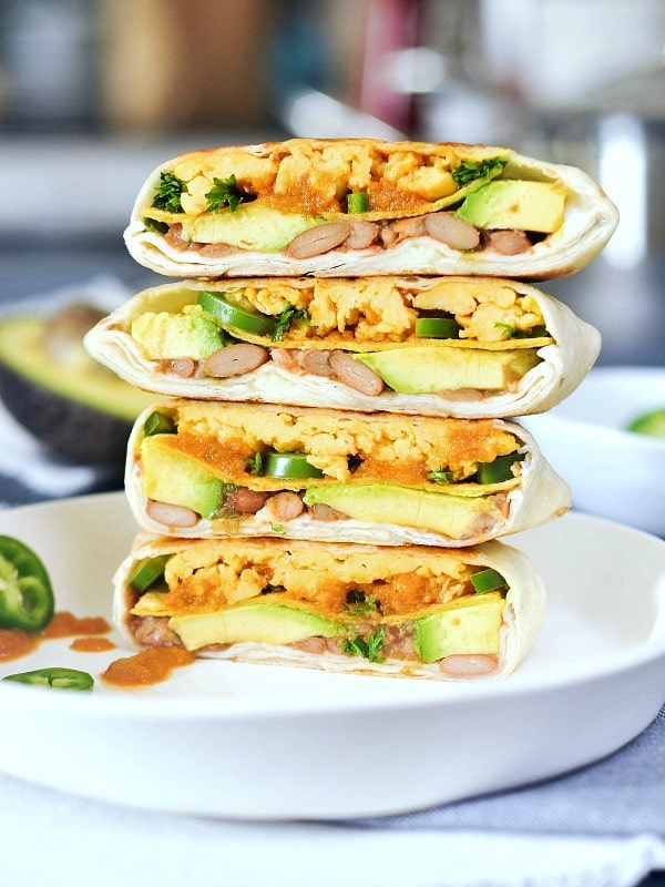 Two ranchero style breakfast crunchwraps sliced in half and stacked four high on a white dish. Crunchwrap is filled with scrambled egg, beans, ranchero sauce, jalapenos.