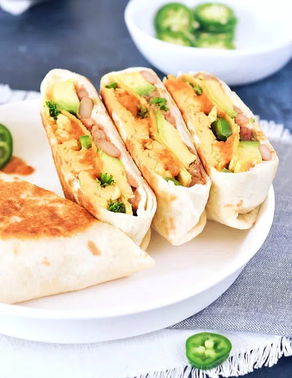 Two ranchero style breakfast crunchwraps sliced in half and arrranged on a white dish. Crunchwrap is filled with scrambled egg, beans, ranchero sauce, jalapenos.