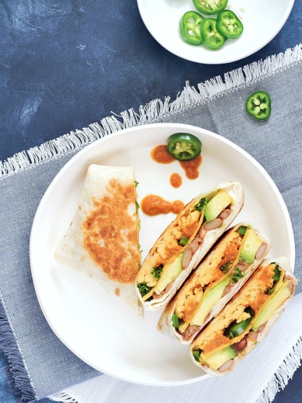 Overhead view of two ranchero style breakfast crunchwraps sliced in half and arrranged on a white dish. Crunchwrap is filled with scrambled egg, beans, ranchero sauce, jalapenos.