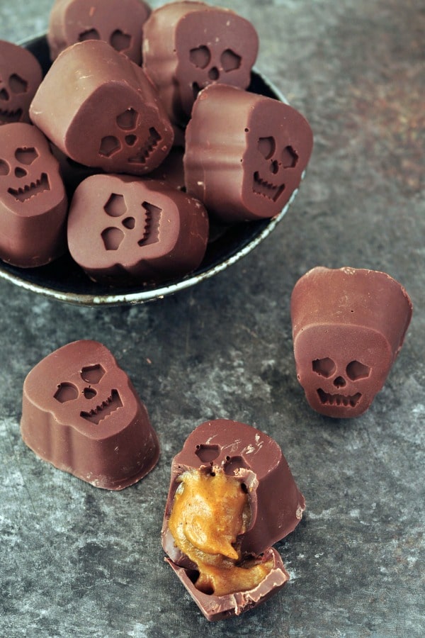 bite size, skull shaped Halloween chocolates stuffed with pumpkin caramel in a bowl, one cut in half to show caramel inside